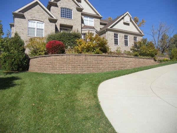 Curved modular block retaining wall in a tan and brown blend, and a concrete driveway curves to the right.